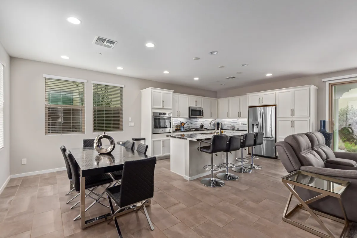 A contemporary interior with a dining table set near a kitchen island and bar stools, seamlessly adjoining a comfortable living area. The scene is brightly lit, with a warm and inviting mood that suggests both everyday family use and the potential for entertaining guests during special occasions.