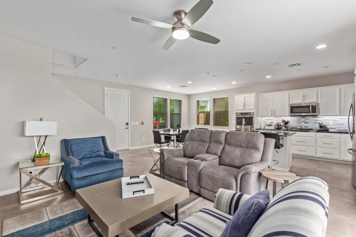 A cozy living area featuring a gray sofa, blue accent chair, modern coffee table, and an open view into the kitchen. The arrangement feels inviting, ideal for relaxing with family or hosting friends, and the open layout promotes connection across spaces.