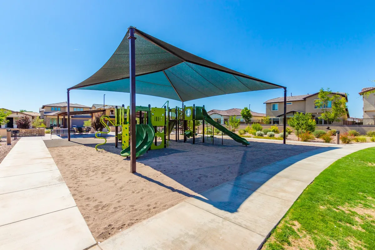 A vibrant playground scene featuring equipment under a shade structure and surrounded by a sand area. Children are depicted playing, while families gather nearby, highlighting a space for laughter and intergenerational fun.