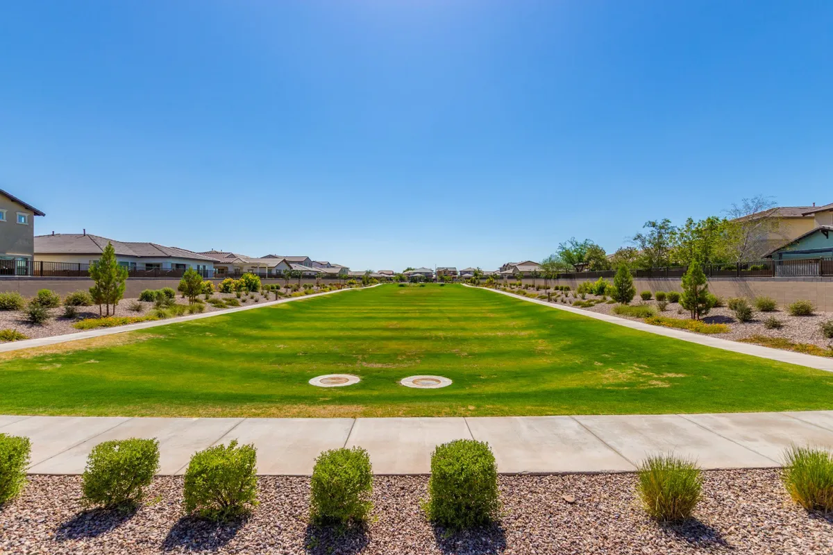 An expansive green lawn with neatly trimmed shrubs and well-maintained pathways offers plenty of room for picnics, outdoor games, and community gatherings. The sunlight and cheerful mood invite families to play and relax together.