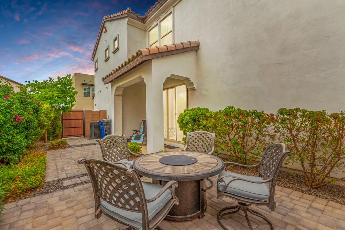 A charming outdoor seating area featuring a paved patio surrounded by lush greenery. Comfortable chairs are arranged around a table, inviting residents to gather, relax with a cup of coffee, or enjoy quiet moments in the sunshine. The ambiance is casual and welcoming, with natural landscaping creating a peaceful retreat.