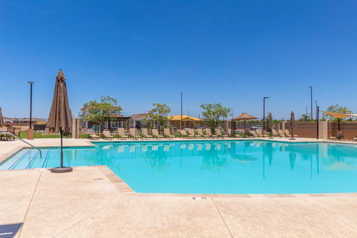 A sparkling community swimming pool is surrounded by sun loungers, umbrellas, and vibrant landscaping. The scene conveys a relaxed and social atmosphere, perfect for families and neighbors to gather on sunny days.