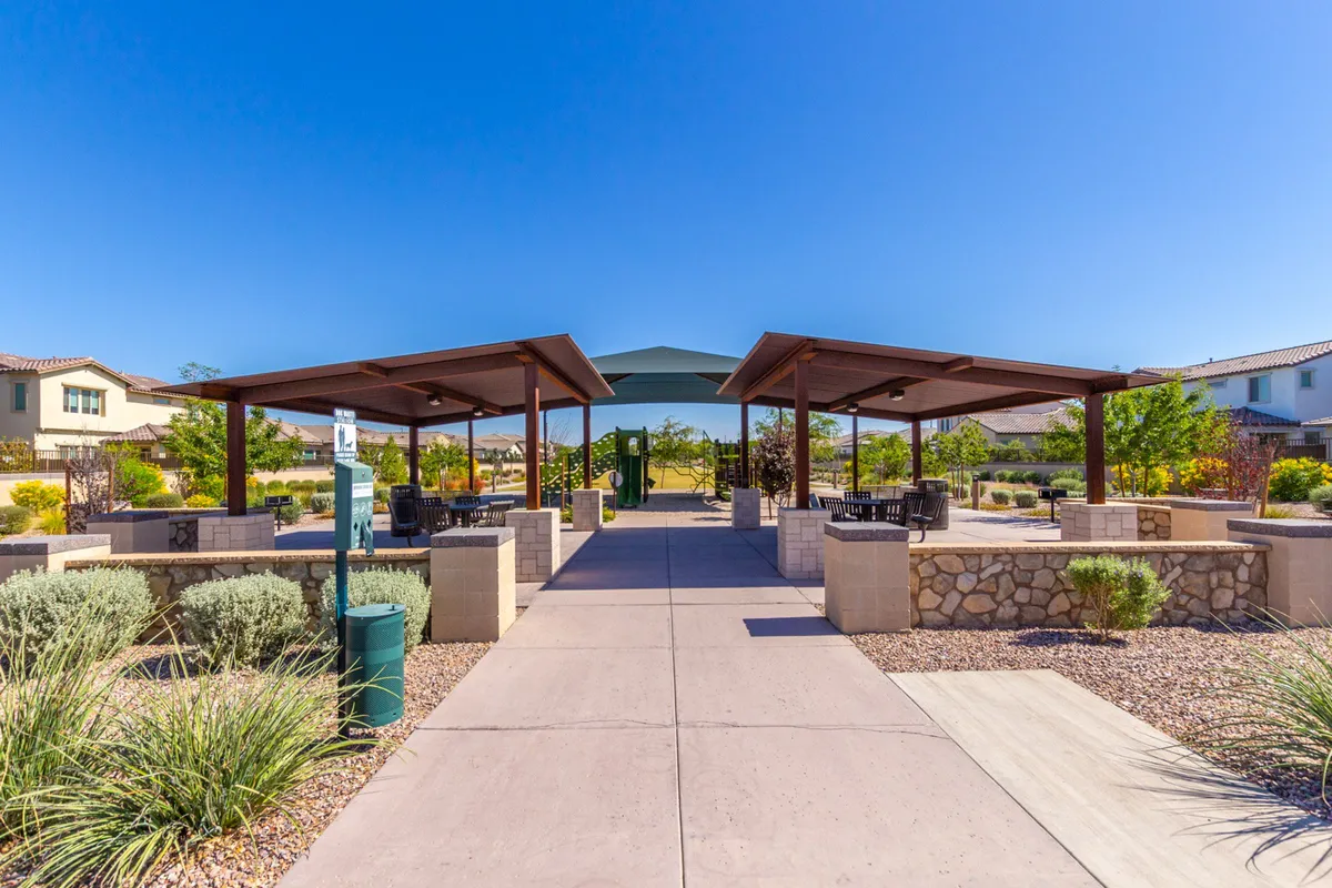 A family-friendly outdoor space featuring shaded pavilions, walkways, and a playground surrounded by well-maintained landscaping. The scene is lively yet peaceful, suggesting a place where families gather for picnics, children play, and community events unfold.