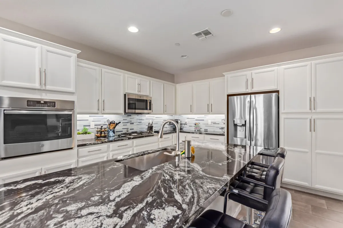 A contemporary kitchen featuring a large central island with a marble countertop, flanked by stainless steel appliances. The island provides ample workspace for group cooking, and the layout is open and inviting for social gatherings.